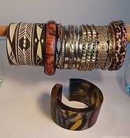 Photo showing assortment of bangles, including black and white patterned, silver tone metal with textured designs, brown animal print bangles, and a chunky hand-painted lucite cuff bracelet with colorful abstract patterns.