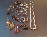 Overall view of all jewelry including pearl necklaces and many pairs of earrings arranged on flat surface