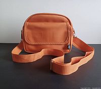 Front view of compact orange bag with flap pocket and adjustable strap