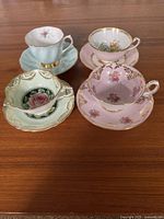 Front view of four tea cups on matching saucers, showing patterns and gilt trim