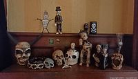 Full view of various skull decor items including horned skull, skull belt, and skeleton figurines displayed on a wooden surface against yellow wall