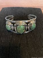 Front view of men's three-stone sterling silver cuff bracelet with greenish oval stones and feather engravings
