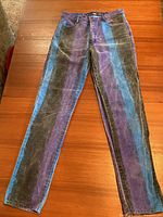Front view of men's vertical band dyed denim jeans laid flat. Denim featuring broad vertical black, purple and blue stripes.