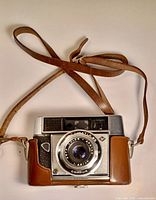 Front view of Agfa Agfamatic Compur camera with brown leather case and strap attached.