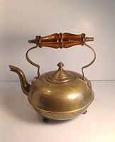 Front view of the vintage brass teapot showing rounded body, curved spout, brass lid with finial, and amber glass handle attached to brass supports.