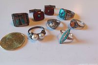 Overview of six rings and pair of cufflinks with size reference coin on white background