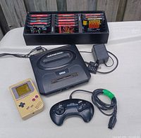 Overhead shot showing Sega Genesis console, controller, power adapter, Game Boy and tray of game cartridges