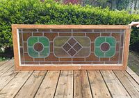 Full view of stained glass window showing wood frame and colored geometric panes in green, pink, amber, and clear glass.