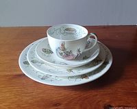 Stacked view of the place setting including cup, saucer, and three plates, showing detailed character illustrations on each piece.