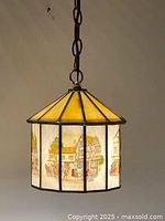 Full view of the stained glass hanging lamp with an octagonal shape showing yellow top panels and illustrated side panels of village scenes.
