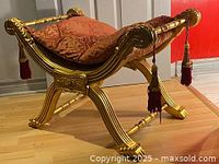 Side angle view of the antique Empire style gilded wooden bench showing red upholstery and curved detailed legs with tassels.