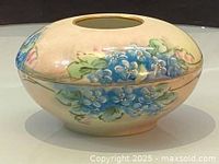 Side view of beige oval Limoges porcelain hair receiver showing blue floral decoration and gold rim on opening.