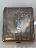 Top view showing the engraved floral design with an oval cartouche on the cigarette case lid.