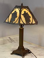Full view of the lamp showing the bronze-tone metal base and glowing slag glass shade with metal relief figures.
