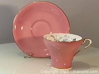 Front view of the pink Aynsley corset teacup with matching saucer in the background.