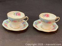 Two Foley Cornflower teacups on matching saucers shown from a frontal angle on black surface.