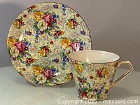 Close-up front view of saucer displaying dense roses time chintz floral pattern.