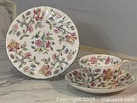 Cake plate, cup, and saucer, all with floral patterns and scalloped edges, displayed on marble surface.
