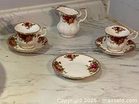 Wide shot showing two Royal Albert Old Country Roses teacups with saucers, one small floral dish, and large creamer pitcher on a marble surface.