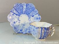 Side view of the blue and white porcelain cup with matching saucer, showing floral patterns, scalloped edges, and gold rim.