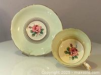 Photo showing both the dish and teacup side by side, highlighting the floral hand-painted rose design and gold trim details.