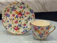Teacup and saucer displayed side by side showing detailed chintz floral pattern and gold trim.
