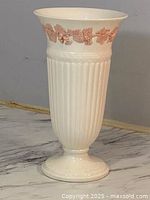 Side view of the tall white fluted ceramic vase with pink floral decoration around the rim