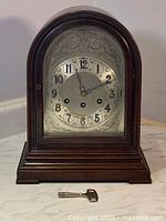 Front view of the mantel clock with closed glass door and winding key resting in front.