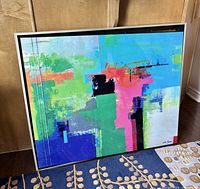 Framed abstract art print leaning against a wall showing colorful abstract shapes and signed 'Neil Young' in bottom right.