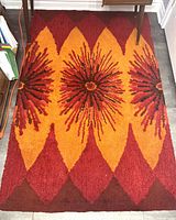 Top view of vintage area rug showing full length and pattern detail with bright orange and red sunburst design and diamond shapes around edges.