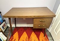 Front view of the vintage mid century small wood laminate desk showing wood grain top, tapered legs and two drawers with metal handles.