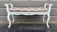 Front view of vintage white wooden hallway bench with upholstered patterned seat placed outdoors against a garage door