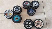 Eight collectible hockey pucks arranged in two rows showing team logos, commemorative event logos and dates.