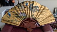 Full view of large folding Asian fan with hand painted birds and lotus motif on gold background