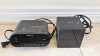 Photo showing Sony ICF-C218 Dream Machine clock radio and Sony battery charger side by side on floor.