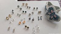 Various pairs of costume earrings arranged next to the butterfly trinket box on a white surface.