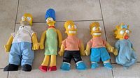 Five vintage Burger King Simpsons plush dolls displayed on floor: Homer, Marge, two Barts, and Lisa.