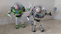Two Buzz Lightyear vintage toys from 1995, one in classic colors and one in silver variation, standing side by side on floor.