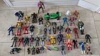 Wide shot showing all vintage action figures, including humanoid and creature figures with varied colors, costumes, and accessories, plus green model slot car on floor against wall.