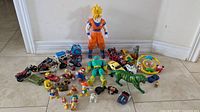Wide shot showing the full collection of vintage toys spread on floor including Dragon Ball Z figure, Battle Cat, Mysterio, vehicles, and other figures.