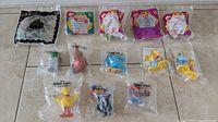 Overview of 10 toys laid out on a surface including Sesame Street PVC figures and McDonald's toys all sealed in original bags