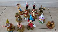 Overview photo showing 12 assorted Disney character figurines from the '90 Years of Magic' collection on circular bases with character names and series branding.
