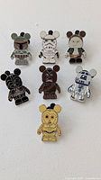 Full set of 7 Vinylmation Star Wars enamel pins featuring Boba Fett, Stormtrooper, Han Solo, Chewbacca, Darth Vader, R2-D2, and C-3PO pins on display surface.