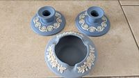 Photo showing the two blue Wedgwood Jasperware candle holders with white relief decoration and the vintage Ecanada Art Pottery ashtray all placed on a tile floor.