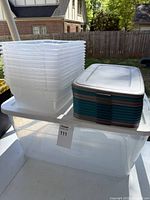 Large clear plastic storage bin with white lid, holding the stack of 12 smaller bins beside it