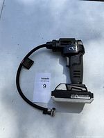 Photo of the cordless air pump showing the side with the hose and battery attached, outdoors on a white surface.