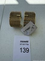 Photo of two wide gold-tone mesh clip-on bracelets displayed on a white surface with a MaxSold tag showing lot number 139.