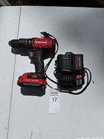 Craftsman cordless drill with battery attached and charger on white surface under sunlight.