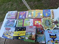Photo showing the full lot of kids games, puzzles, and books arranged on a table outside on grass.