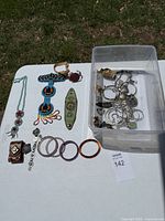 Overview of all jewelry items laid out on white surface, including bracelets, hoop earrings, necklace, and bin with assorted pieces.